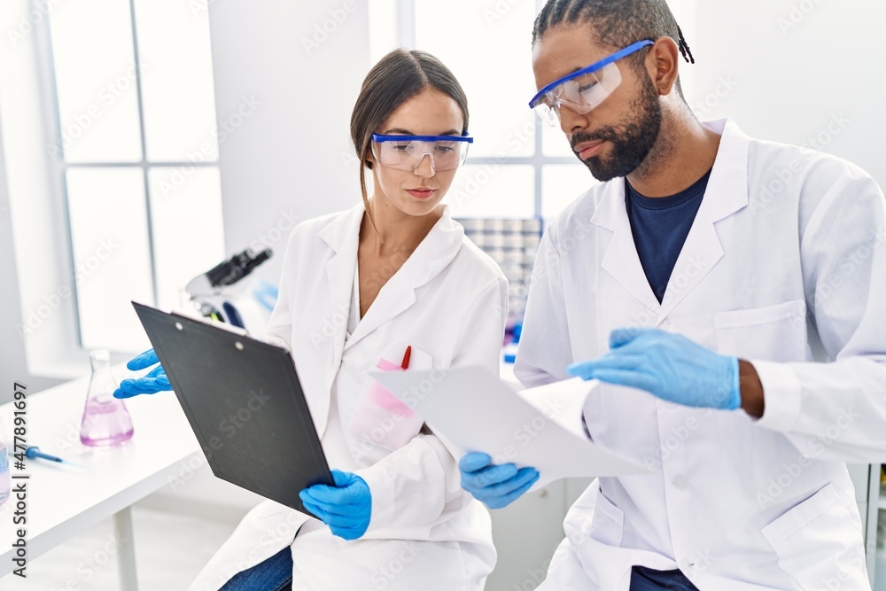 Man and woman scientist partners reading documents at laboratory Man and woman scientist partners reading documents at laboratory