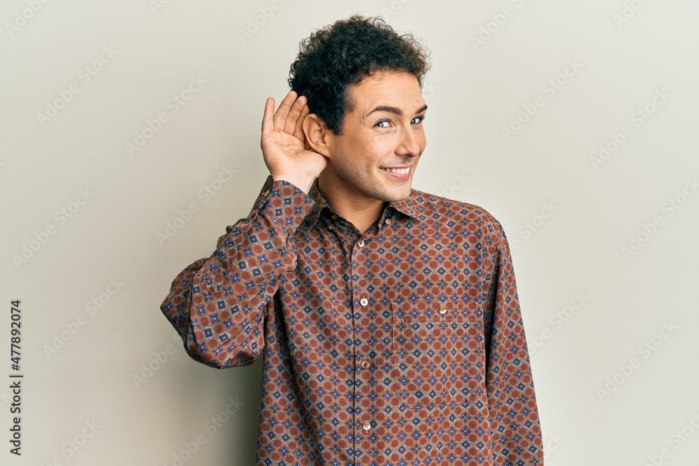 Handsome hispanic man wearing casual clothes smiling with hand over ear listening an hearing to rumor or gossip. deafness concept. Handsome hispanic man wearing casual clothes smiling with hand over ear listening an hearing to rumor or gossip. deafness concept.