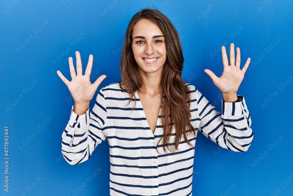 Young hispanic woman standing over blue isolated background showing and pointing up with fingers number ten while smiling confident and happy. Young hispanic woman standing over blue isolated background showing and pointing up with fingers number ten while smiling confident and happy.