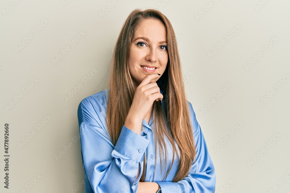 Young blonde woman wearing casual blue shirt looking confident at the camera with smile with crossed arms and hand raised on chin. thinking positive. Young blonde woman wearing casual blue shirt looking confident at the camera with smile with crossed arms and hand raised on chin. thinking positive.