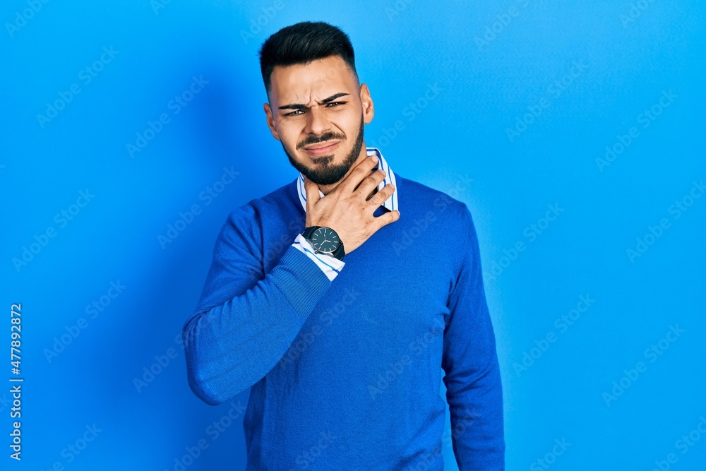 Young hispanic man with beard wearing casual blue sweater touching painful neck, sore throat for flu, clod and infection Young hispanic man with beard wearing casual blue sweater touching painful neck, sore throat for flu, clod and infection