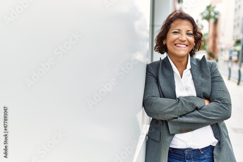 Photographie Middle age latin businesswoman smiling happy standing with arms crossed gesture at the city