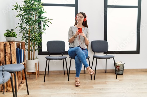 Young asian woman sitting wearing headphones at waiting room