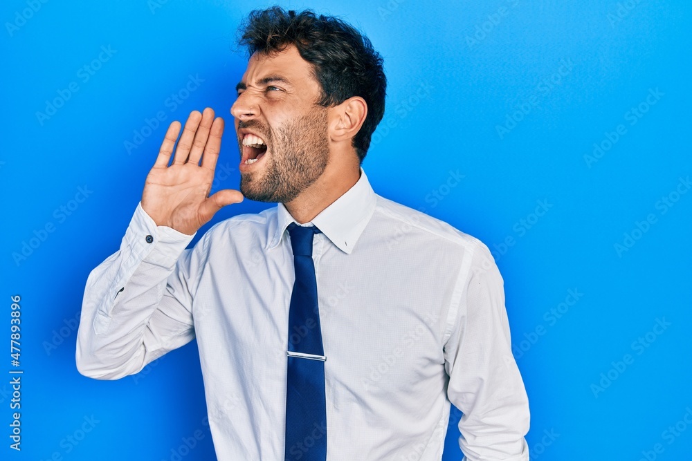 Handsome man with beard wearing business shirt and tie shouting and screaming loud to side with hand on mouth. communication concept. Handsome man with beard wearing business shirt and tie shouting and screaming loud to side with hand on mouth. communication concept.