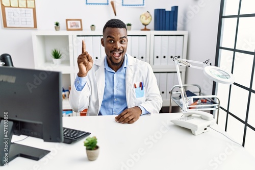 Young african doctor man wearing stethoscope at the clinic pointing finger up with successful idea. exited and happy. number one.