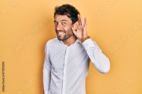 Handsome man with beard wearing casual white t shirt smiling with hand over ear listening and hearing to rumor or gossip. deafness concept. photo