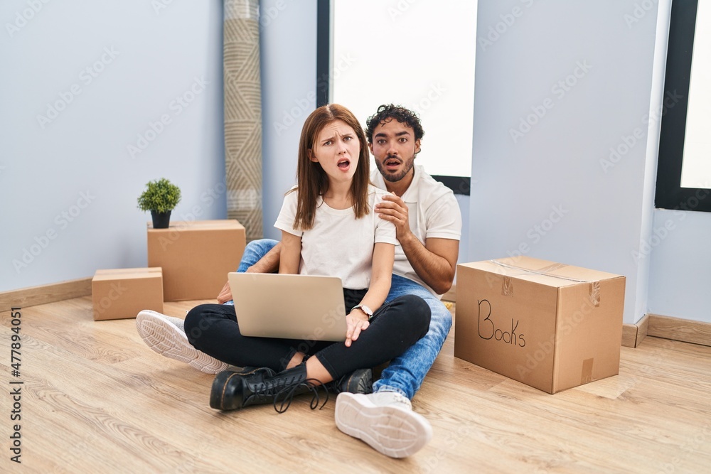 Young couple using laptop at new home in shock face, looking skeptical and sarcastic, surprised with open mouth Young couple using laptop at new home in shock face, looking skeptical and sarcastic, surprised with open mouth