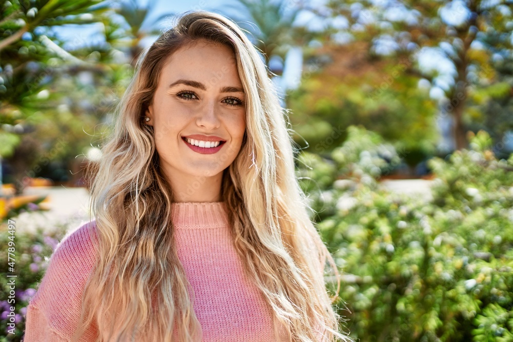 Young blonde woman smiling at the park - obrazy, fototapety, plakaty 