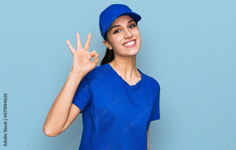 Young hispanic girl wearing delivery courier uniform smiling positive doing ok sign with hand and fingers. successful expression. Young hispanic girl wearing delivery courier uniform smiling positive doing ok sign with hand and fingers. successful expression.