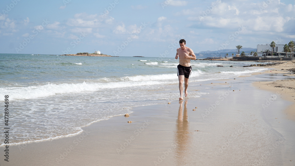 Young man jogging on a sandy beach on a sunny day in Malia, Crete Island of Greece. Young man jogging on a sandy beach on a sunny day in Malia, Crete Island of Greece.