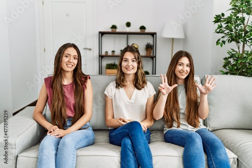 Group of three hispanic girls sitting on the sofa at home showing and pointing up with fingers number eight while smiling confident and happy.