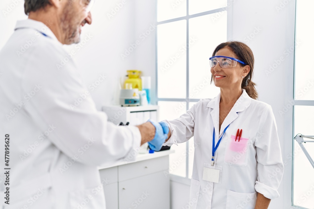 Middle age man and woman partners wearing scientist uniform shake hands at laboratory Middle age man and woman partners wearing scientist uniform shake hands at laboratory