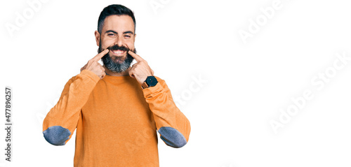 Hispanic man with beard wearing casual winter sweater smiling with open mouth, fingers pointing and forcing cheerful smile