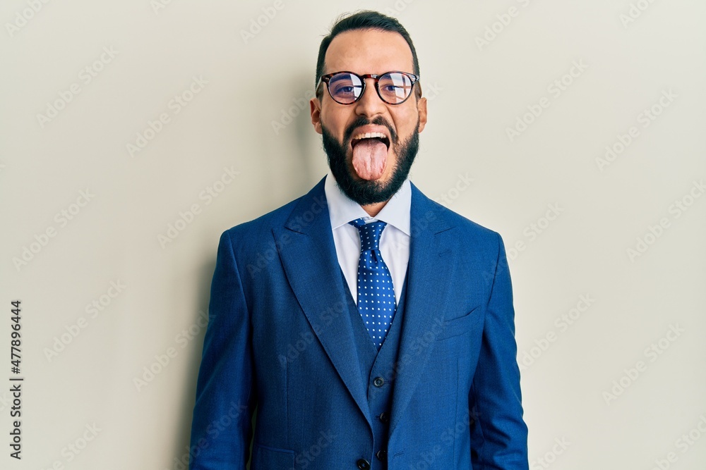 Young man with beard wearing business suit and tie sticking tongue out happy with funny expression. emotion concept. Young man with beard wearing business suit and tie sticking tongue out happy with funny expression. emotion concept.