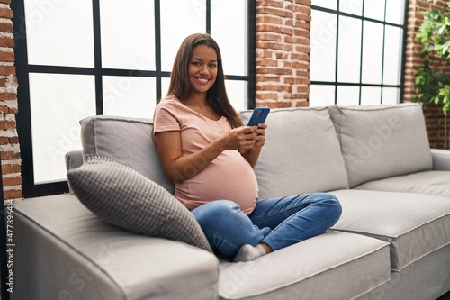 Young latin woman pregnant using smartphone at home