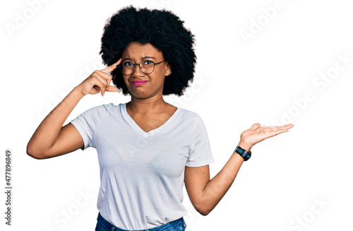 Young african american woman wearing casual white t shirt confused and annoyed with open palm showing copy space and pointing finger to forehead. think about it.