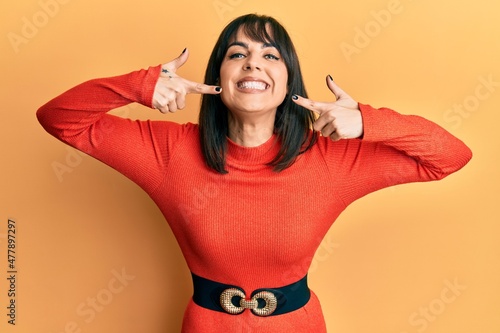 Young hispanic woman wearing casual clothes smiling cheerful showing and pointing with fingers teeth and mouth. dental health concept.