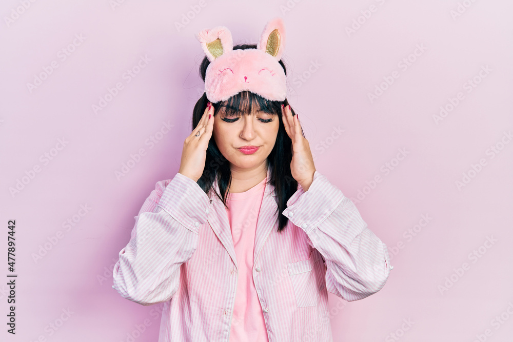Young hispanic woman wearing sleep mask and pajama suffering from headache desperate and stressed because pain and migraine. hands on head. Young hispanic woman wearing sleep mask and pajama suffering from headache desperate and stressed because pain and migraine. hands on head.