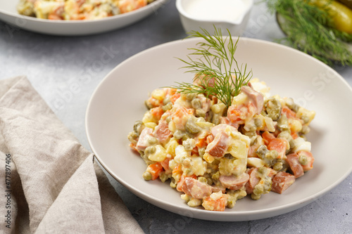 traditional east european dish for New Year's Eve - salad "Olivier" with potatoes, carrots, onion, peas, sausage, cucumbers, eggs and mayonnaise in a grey bowl