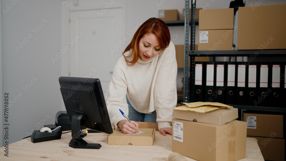 Young redhead woman ecommerce business worker writing on package at office Young redhead woman ecommerce business worker writing on package at office
