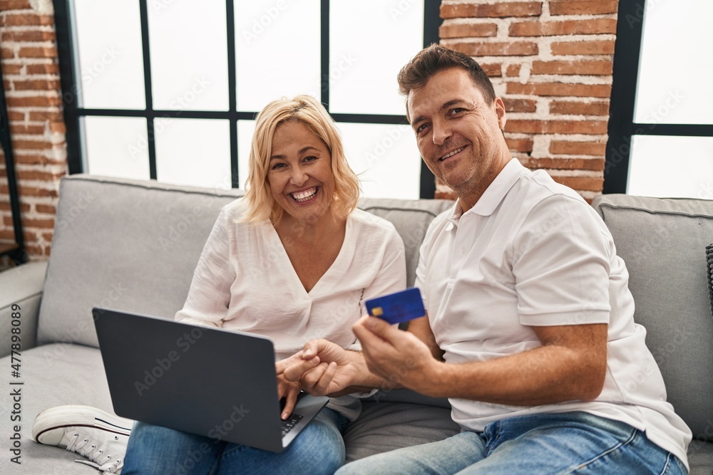 Fototapeta premium Middle age man and woman using laptop and credit card sitting on sofa at home