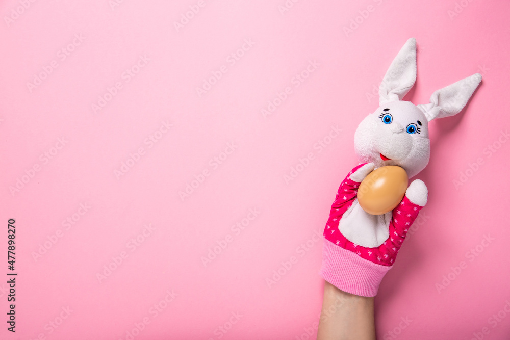 Banner with white bunny and egg in hands on pink background with copy space, empty text place. Christian holiday card Happy Easter. Online toy theater course. Hand puppet. Traditional childhood play. Banner with white bunny and egg in hands on pink background with copy space, empty text place. Christian holiday card Happy Easter. Online toy theater course. Hand puppet. Traditional childhood play.