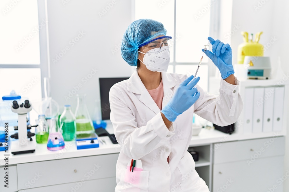 Young latin woman wearing scientist uniform holding vaccine at laboratory Young latin woman wearing scientist uniform holding vaccine at laboratory