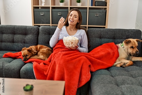 Photography Young hispanic woman watching movie sitting on sofa with dogs at home