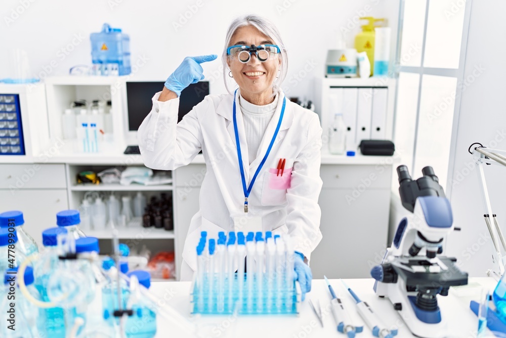 Middle age grey-haired woman wearing scientist uniform smiling happy pointing with hand and finger