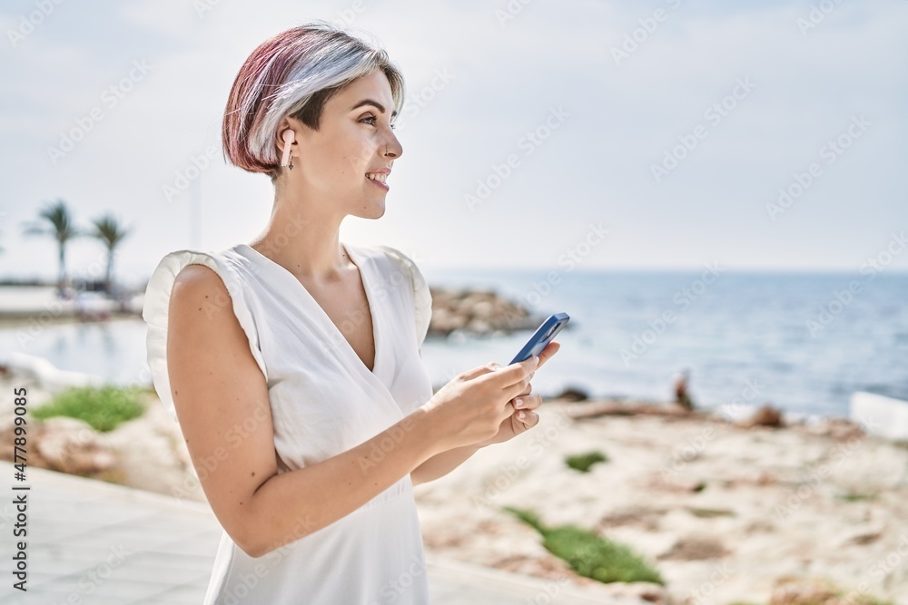 Young caucasian girl smiling happy using earphones and smartphone at the beach.