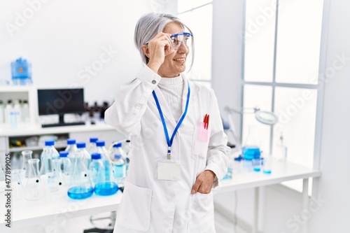 Middle age grey-haired woman wearing scientist uniform smiling confident at laboratory