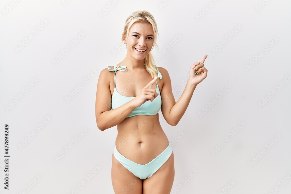 Young caucasian woman wearing bikini over isolated background smiling and looking at the camera pointing with two hands and fingers to the side. Young caucasian woman wearing bikini over isolated background smiling and looking at the camera pointing with two hands and fingers to the side.