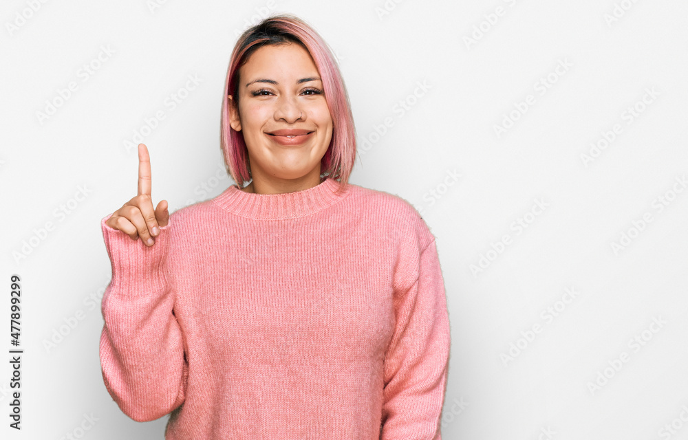 Hispanic woman with pink hair wearing casual winter sweater showing and pointing up with finger number one while smiling confident and happy. Hispanic woman with pink hair wearing casual winter sweater showing and pointing up with finger number one while smiling confident and happy.