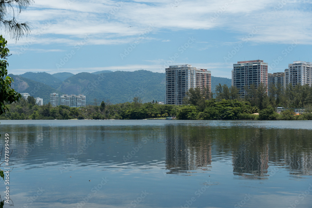 View of the Marapendi lagoon with buildings in the background and surrounding vegetation and trees. Hills in the background. Located near Praia da Reserva in Rio de Janeiro