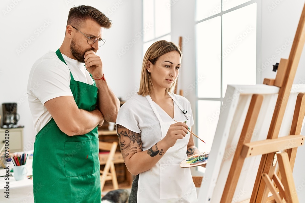 Young caucasian couple with serious expression drawing at art studio. Man standing and looking draw canvas. Young caucasian couple with serious expression drawing at art studio. Man standing and looking draw canvas.