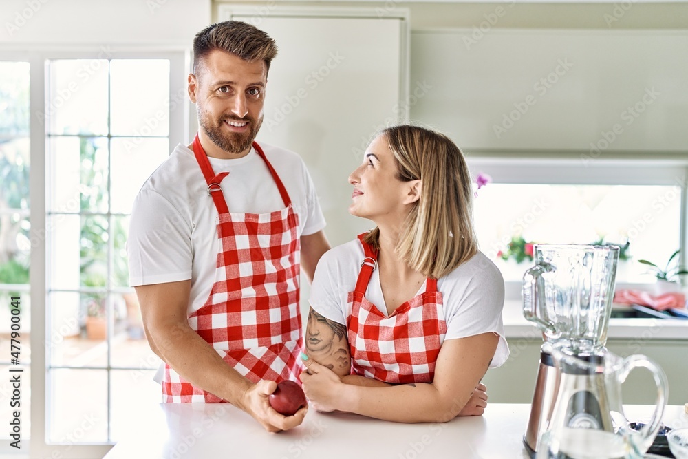 Young couple smiling confident holding red apple at kitchen Young couple smiling confident holding red apple at kitchen