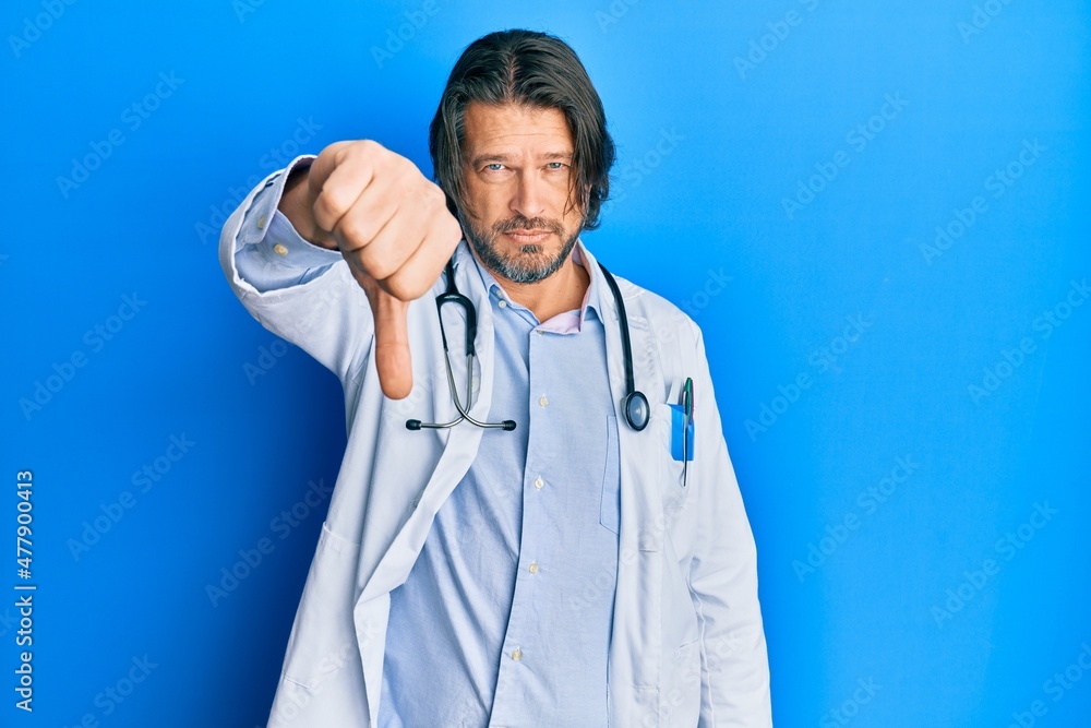 Middle age handsome man wearing doctor uniform and stethoscope looking unhappy and angry showing rejection and negative with thumbs down gesture. bad expression. Middle age handsome man wearing doctor uniform and stethoscope looking unhappy and angry showing rejection and negative with thumbs down gesture. bad expression.