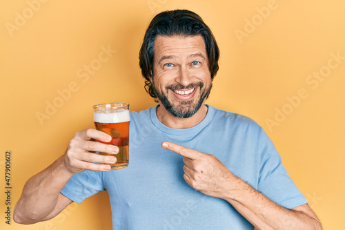 Middle age caucasian man drinking a pint of beer smiling happy pointing with hand and finger