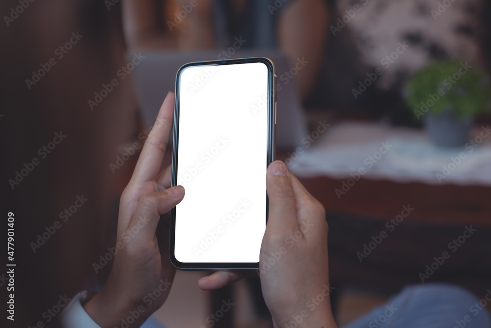 Cell phone mockup image blank white screen.  Woman hand holding, using mobile phone in coffee shop, close up