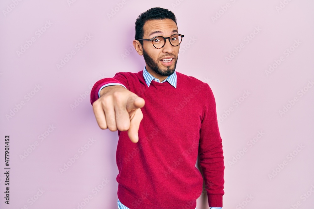 Hispanic man with beard wearing business shirt and glasses pointing displeased and frustrated to the camera, angry and furious with you Hispanic man with beard wearing business shirt and glasses pointing displeased and frustrated to the camera, angry and furious with you