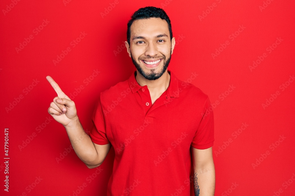Hispanic man with beard pointing with fingers to the side smiling with a happy and cool smile on face. showing teeth. Hispanic man with beard pointing with fingers to the side smiling with a happy and cool smile on face. showing teeth.