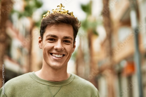 Young hispanic man smiling happy wearing gold king crown at the city.
