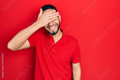 Hispanic man with beard wearing casual red t shirt smiling and laughing with hand on face covering eyes for surprise. blind concept. © Krakenimages.com