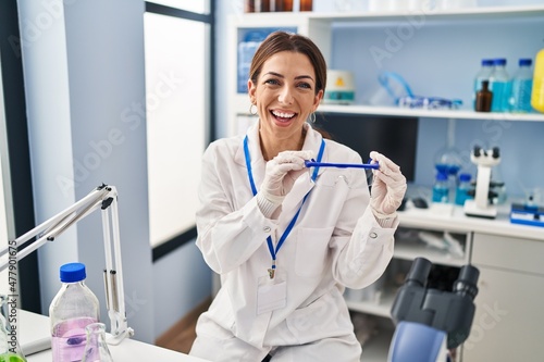 Young brunette woman working at scientist laboratory wearing safety glasses smiling and laughing hard out loud because funny crazy joke.