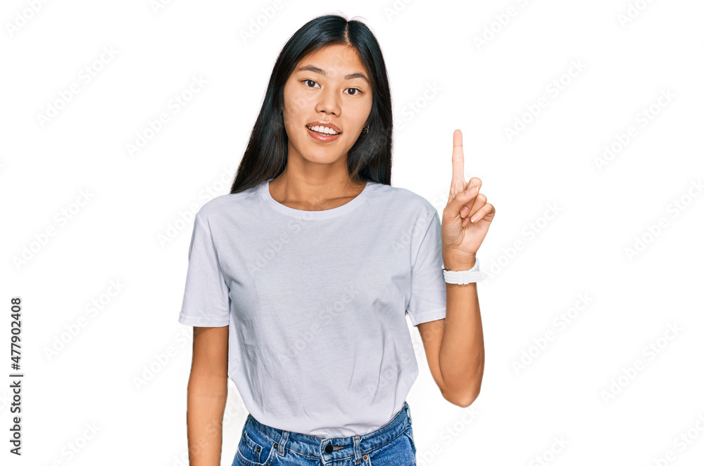 Beautiful young asian woman wearing casual white t shirt pointing finger up with successful idea. exited and happy. number one. Beautiful young asian woman wearing casual white t shirt pointing finger up with successful idea. exited and happy. number one.