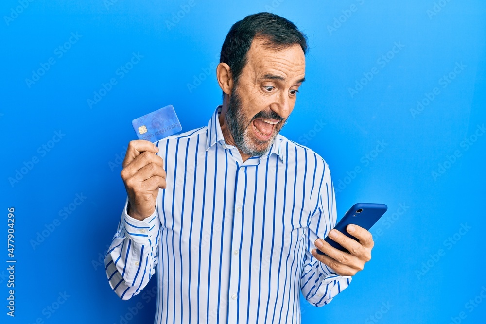 Middle age hispanic man using smartphone and holding credit card celebrating crazy and amazed for success with open eyes screaming excited.