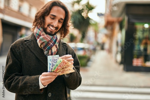Billede på lærred Young hispanic man smiling happy counting canadian dollars at the city