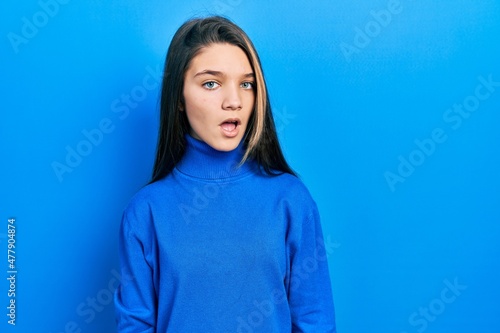 Young brunette girl wearing turtleneck sweater in shock face, looking skeptical and sarcastic, surprised with open mouth