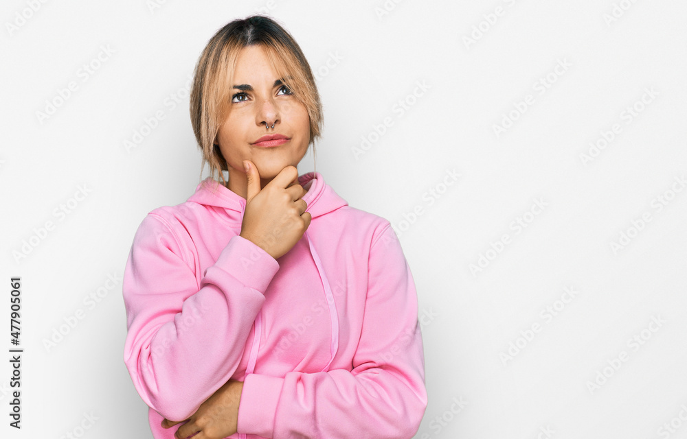 Young caucasian woman wearing casual sweatshirt with hand on chin thinking about question, pensive expression. smiling with thoughtful face. doubt concept. Young caucasian woman wearing casual sweatshirt with hand on chin thinking about question, pensive expression. smiling with thoughtful face. doubt concept.