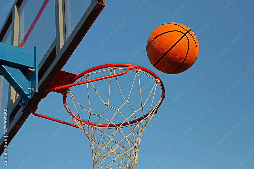 A basketball in a net on a blue sky background. The ball hit the ring. sport. A basketball in a net on a blue sky background. The ball hit the ring. sport.